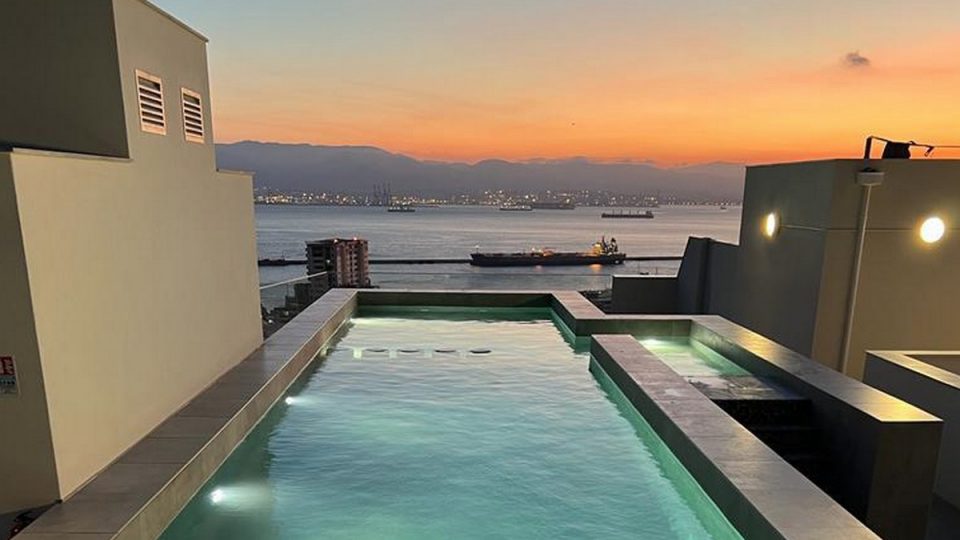 Rooftop infinity pool in Gibraltar’s Upper Town overlooking the Bay of Gibraltar at sunset, with sea views, anchored ships, and modern apartment terraces.